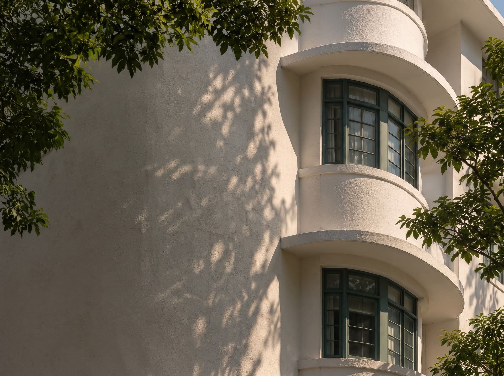 sunlit curved balconies of a Streamline Moderne block with tree shadows, Singapore